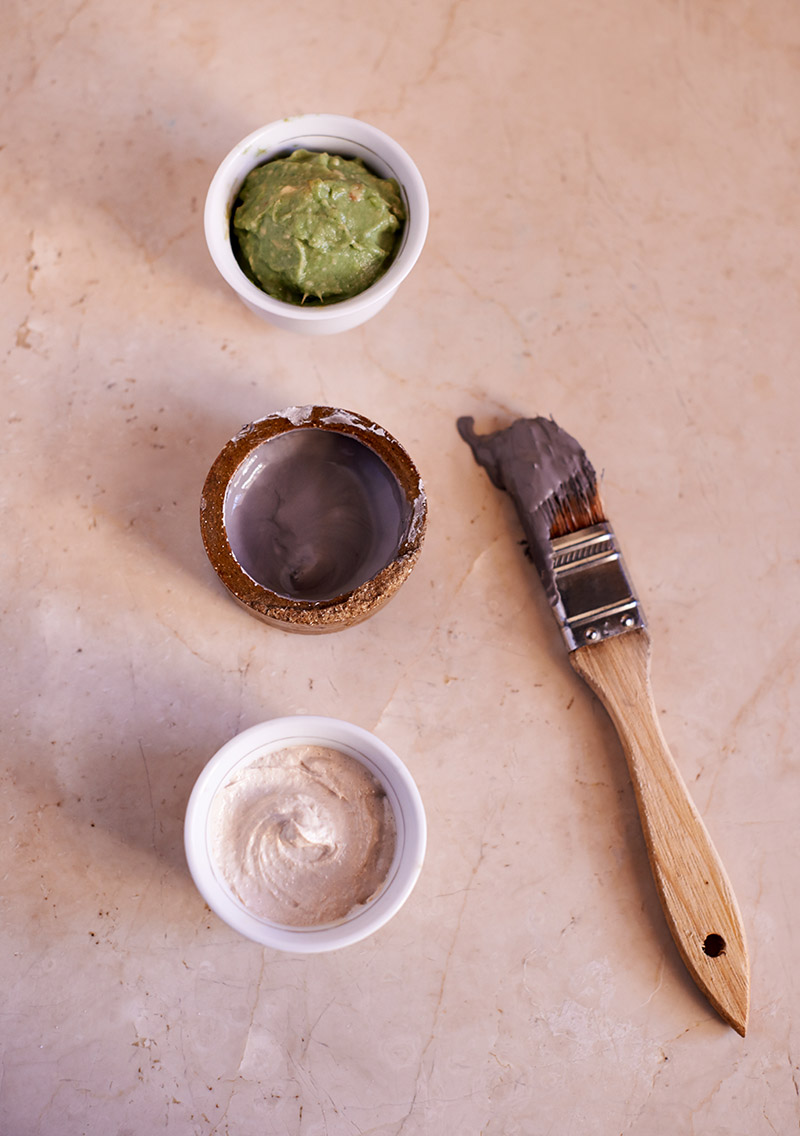 Three containers of different colored pastes with a paintbrush on a marble surface.