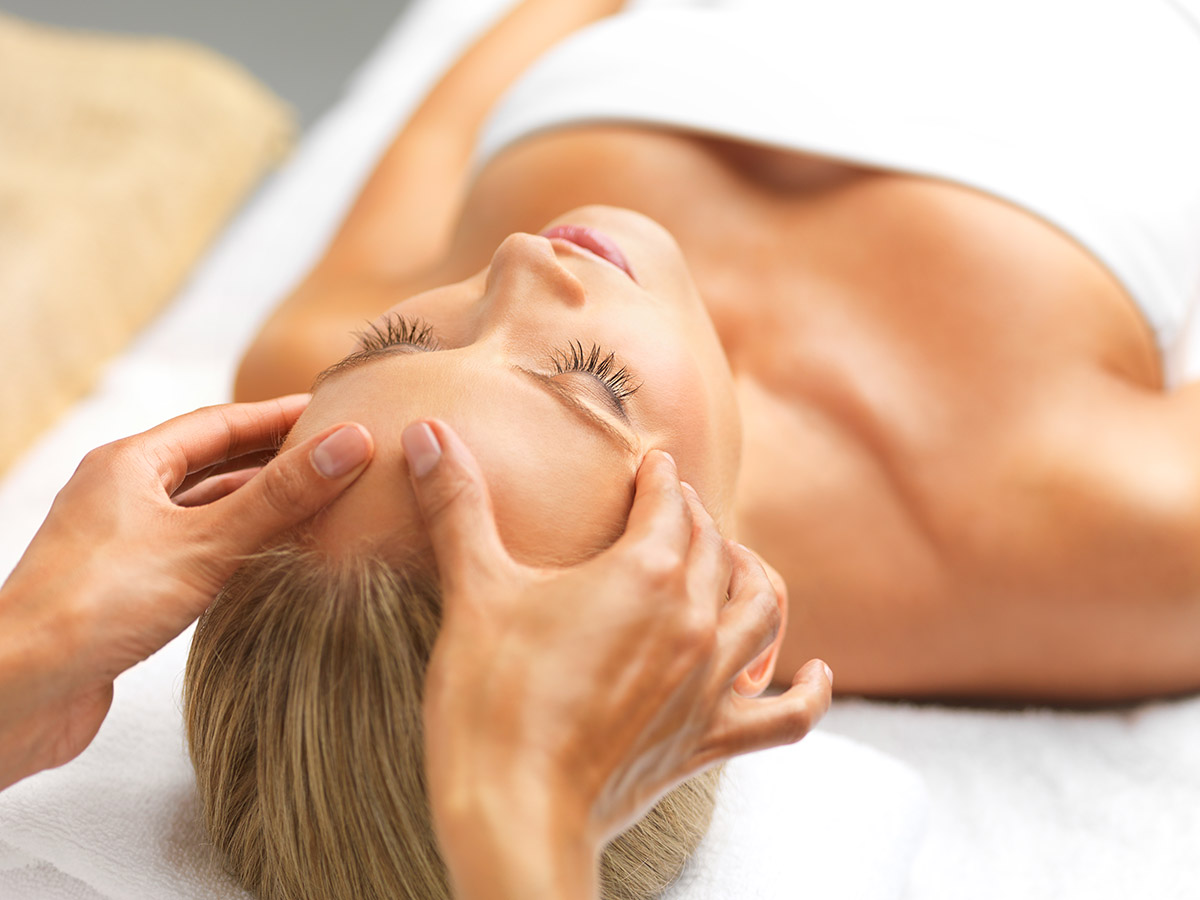 A woman receiving a calming head massage in a spa setting.