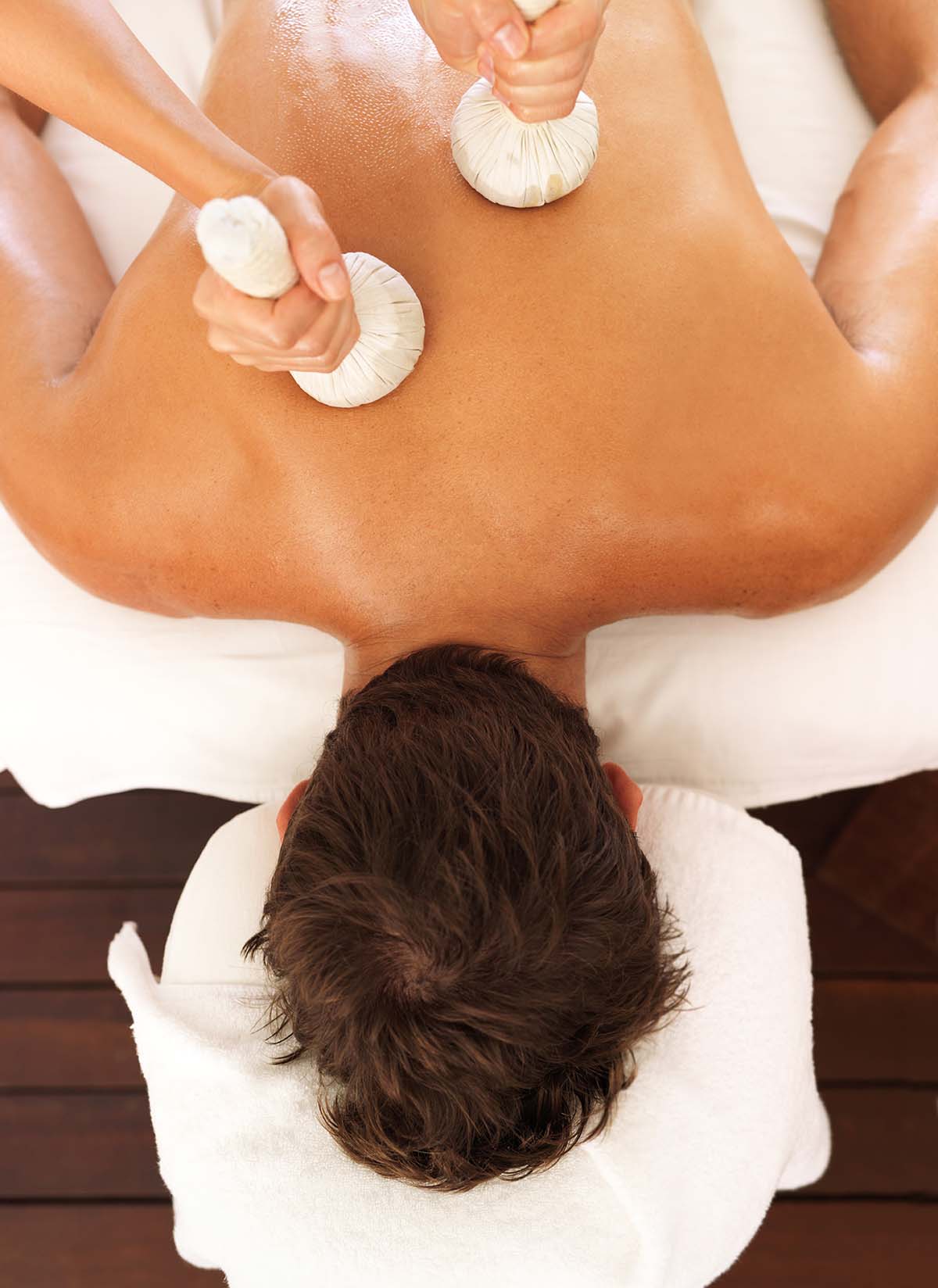 Person receiving herbal compress massage on back.