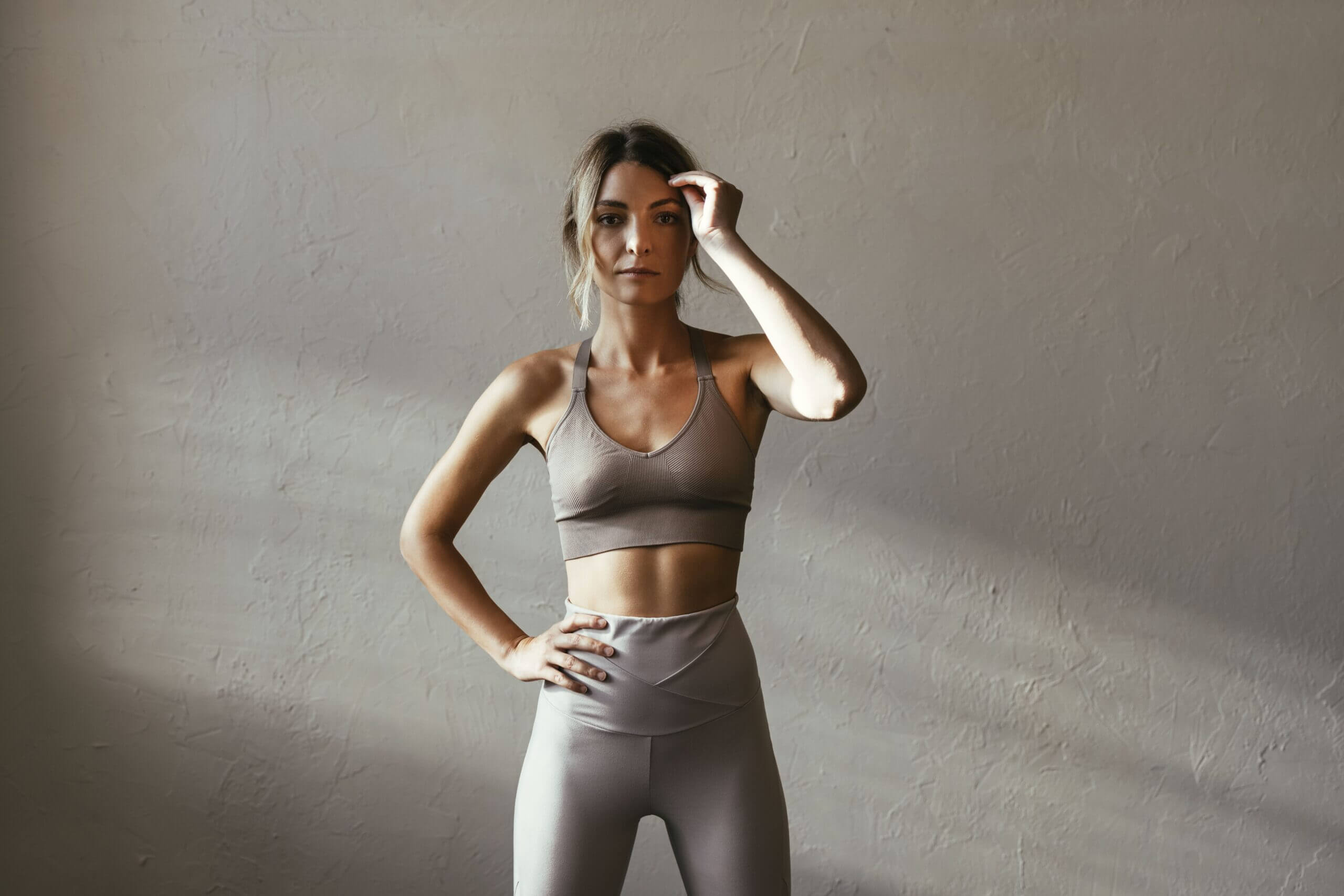 Woman in workout clothes posing against a plain wall.